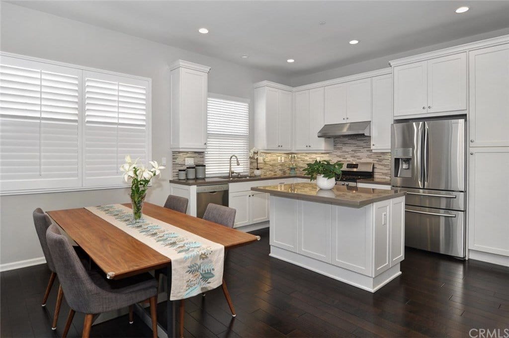 Kitchen and open dining area with stainless steel appliances, large center island and white cabinets. 
