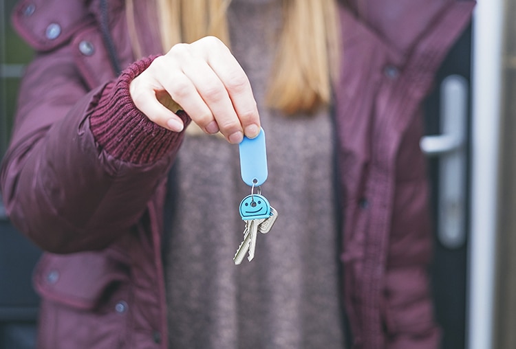 person in purple jacket holding up keys with blue key chain