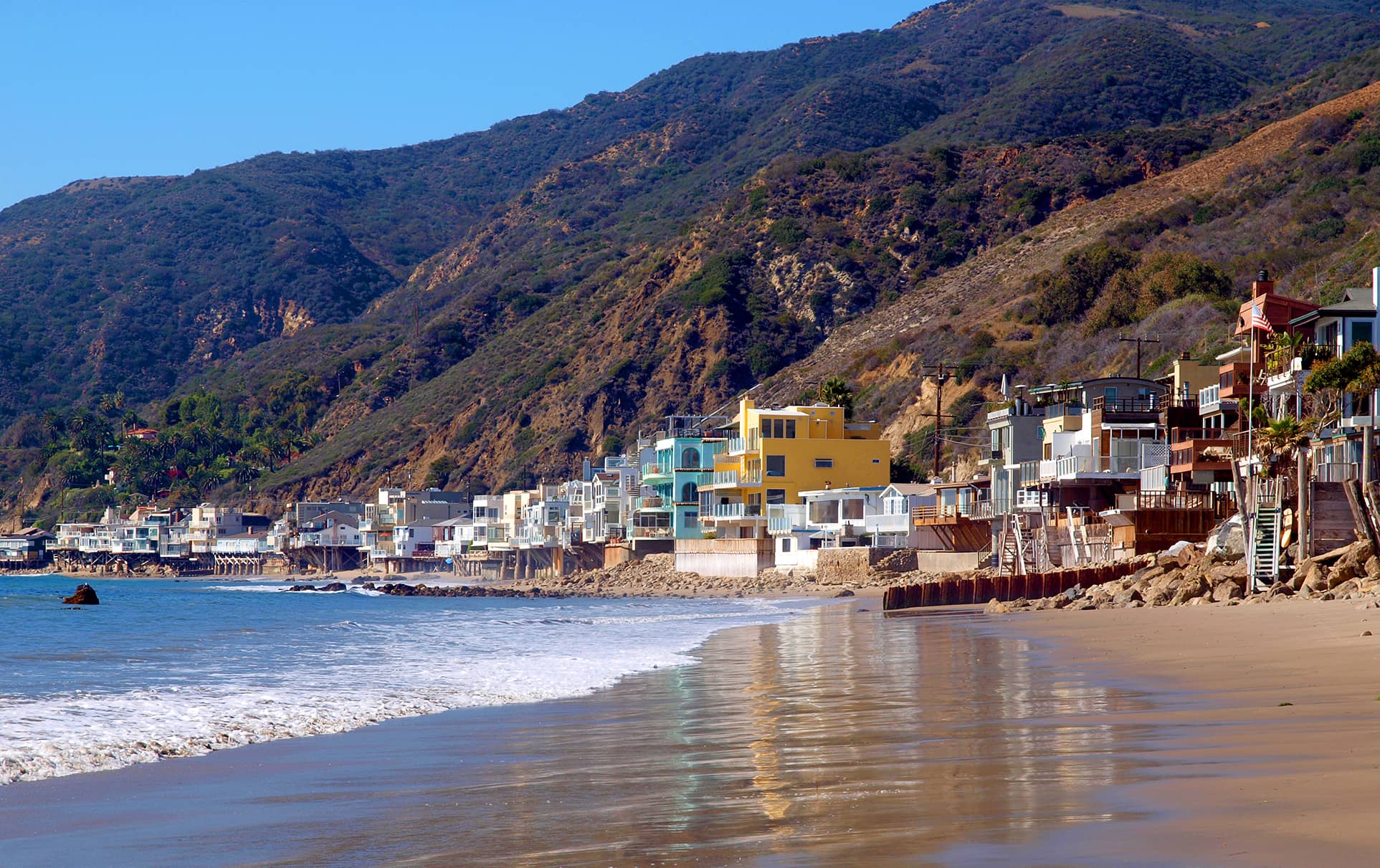 Malibu beach in CA with homes along the sand and rocky cliffs
